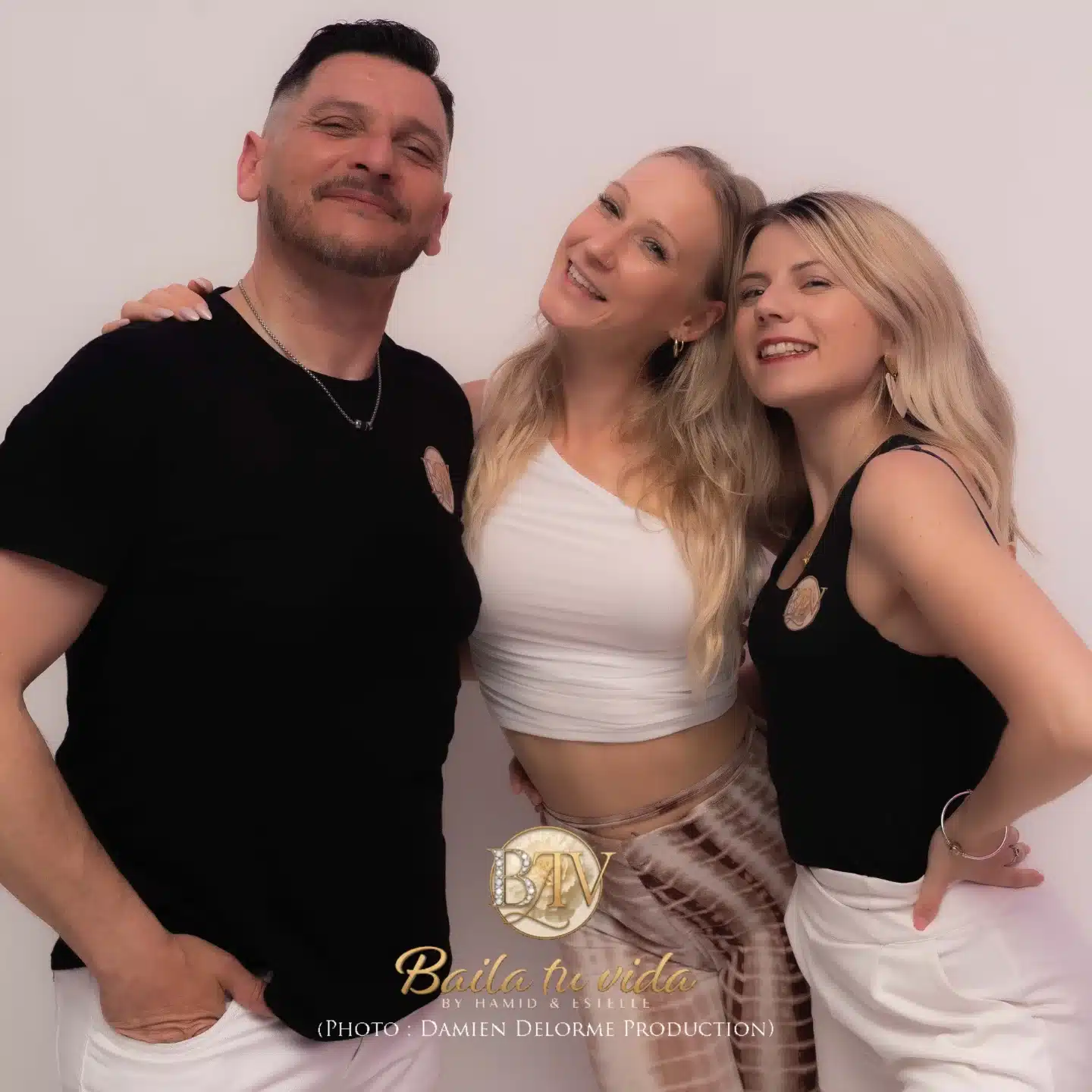 Trois personnes souriantes, un homme et deux femmes, posent. Logo 'Baila tu vida BY HAMID & ESTIELLE (PHOTO : DAMIEN DELORME PRODUCTION)'.
